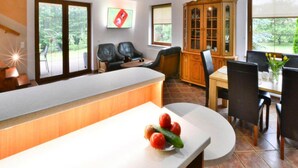 A modern kitchen with a white countertop, a dining area with a wooden table and chairs, and a view of greenery through the windows. - Comfortable Holiday Villa, Swiecianowo (Malechowo)