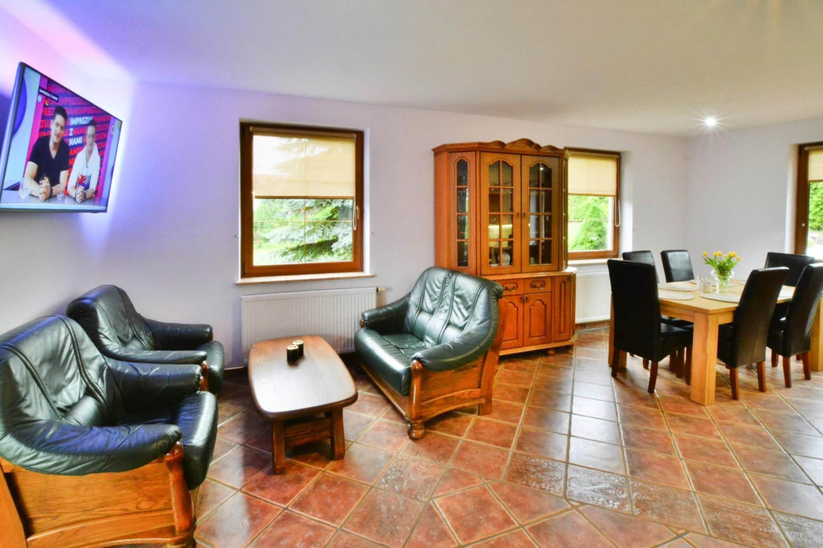 A living room with leather sofas, a wooden cabinet, a dining table with chairs, and a television mounted on the wall.