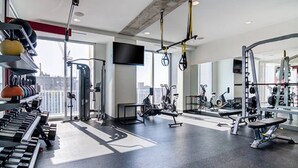 A modern gym with various exercise equipment, large windows, and a city view. - Royal Escape Midtown High Rise (Atlanta)