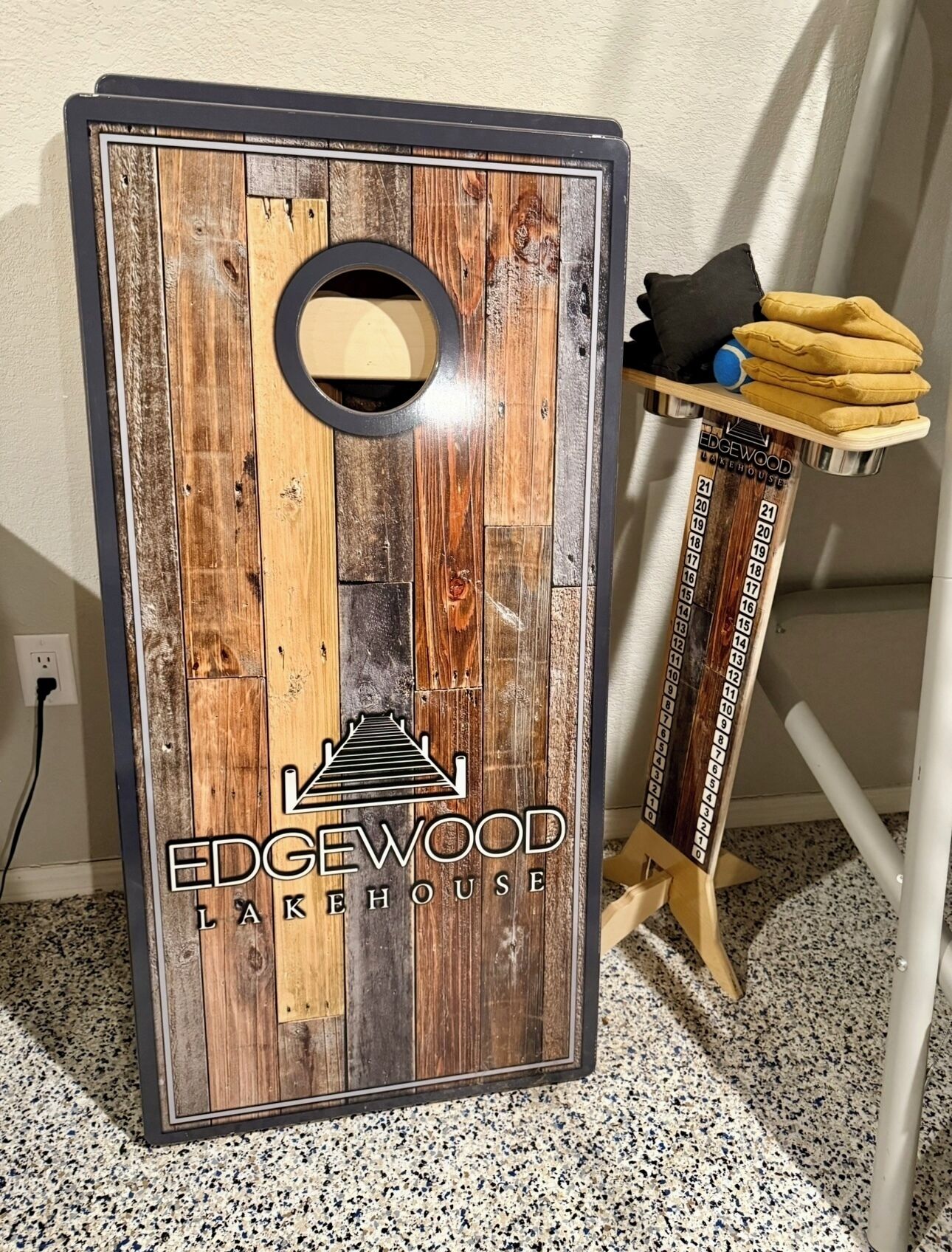 A wooden dartboard with a logo and a number chart, placed on a stand with cushions.