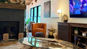A modern living room with a glass coffee table, a fireplace, a television, and a ceiling fan.