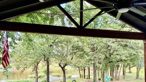 A covered outdoor seating area with a view of a pond and trees.