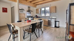 A modern kitchen with wooden beams, a dining area with chairs, and a view of the outdoors through a window.