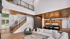 A spacious living area with a wooden staircase, a large sofa, and a dining area with modern kitchenettes. - Modern Mountain Haus - 7 bedroom/5 bath/5 decks/4 fireplaces/Theater - 6195 sqft (Blue Ridge)
