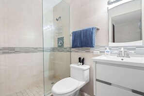 Une salle de bain moderne avec une douche à parois de verre, des toilettes blanches et un lavabo avec un miroir au-dessus.