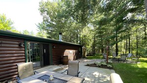A log cabin with a patio area featuring a table and chairs, surrounded by a forested landscape. - Lazy Days @ Spring Brook Resort (Wisconsin Dells)