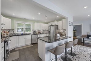 A modern kitchen with white cabinets, a stainless steel refrigerator, and a black countertop.