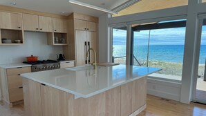 A modern kitchen with wooden cabinets, a central island, and a view of the ocean. - Modern Lake Michigan Private Beach Cottage (Harbor Springs)