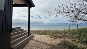 A wooden building with a covered porch overlooking a beach. - Modern Lake Michigan Private Beach Cottage (Harbor Springs)