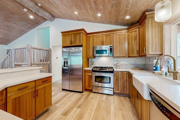 A modern kitchen with wooden cabinets, stainless steel appliances, and a wooden staircase.