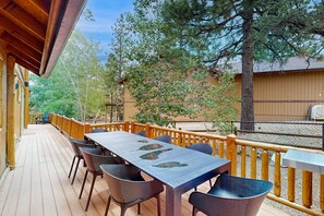 Una terraza de madera con una mesa y sillas, rodeada por barandilla de madera y árboles.