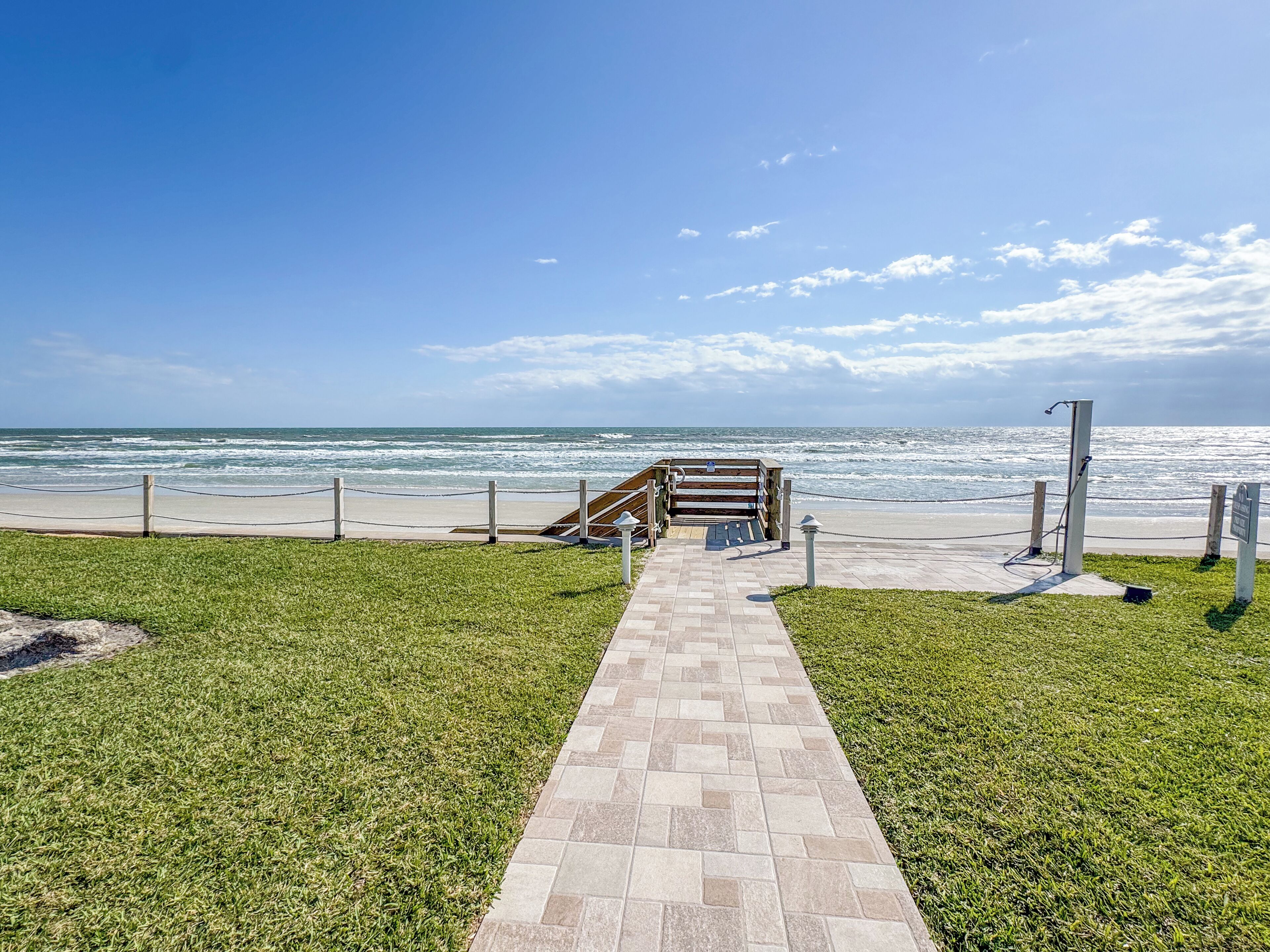 A pathway leading to a beach with a wooden structure and a signpost.