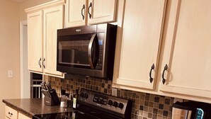 A kitchen with light wooden cabinets, a black microwave, a stainless steel range, and a coffee maker.