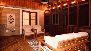 A cozy wooden cabin with a ceiling fan, two cushioned chairs, a wooden bench, and large windows.