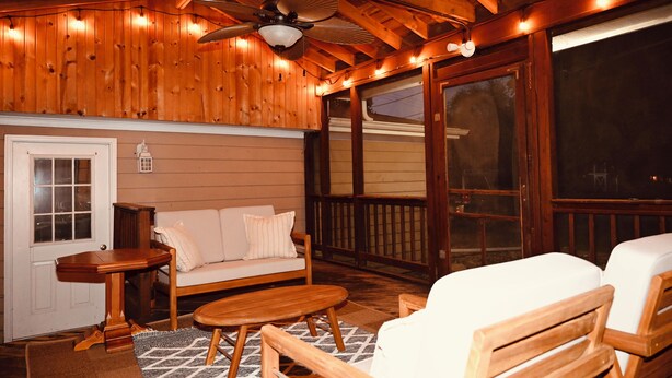 A wooden deck with a ceiling fan, a sofa, and a table.