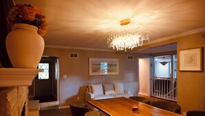 A dining area with a wooden table, chairs, a chandelier, a vase with flowers, and a painting on the wall.