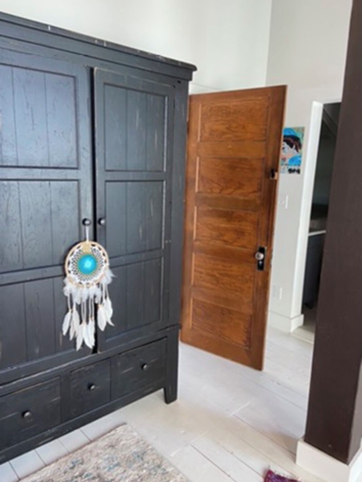 Een donkere houten garderobe met een decoratieve dromenvanger, een houten deur en een betegelde vloer.