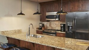 A kitchen with granite countertops, stainless steel appliances, dark wooden cabinets, and pendant lighting.