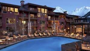 A hotel with a pool, lounge chairs, and a mountain backdrop.