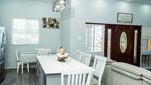 Een moderne keuken met witte kasten, een eettafel met stoelen, een kroonluchter en een decoratief wandobject.