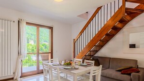 A dining area with a table set for four, a brown sofa, and a wooden staircase. - Nice apartment for 4 people with WIFI, A/C, pool and terrace (Dizzasco)