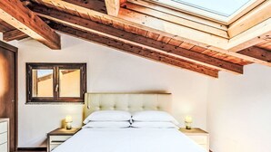 A bedroom with a bed, two bedside tables, a nightstand, a window, and a wooden ceiling. - Nice apartment for 4 people with WIFI, A/C, pool and terrace (Dizzasco)