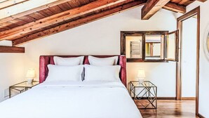 Ein Schlafzimmer mit schrägverdeckter Decke, einem Bett mit weißer Bettwäsche, zwei Nachttischen mit Lampen und einem Spiegel an der Wand.