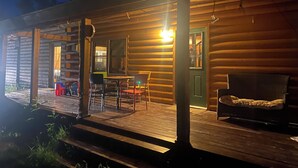 Eine Blockhütte mit einer Holzterrasse, einem Essbereich mit Stühlen und einem Tisch sowie einer grünen Tür.
