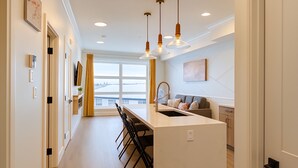 A modern kitchen with a central island, bar stools, pendant lighting, and a view of the city through large windows.