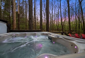 Un bain à remous situé dans un espace boisé, avec une terrasse et des chaises rouges.