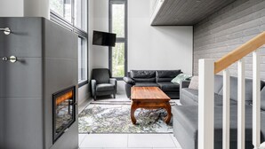 A modern living room with a fireplace, a grey sofa, a wooden coffee table, and a TV mounted on the wall.
