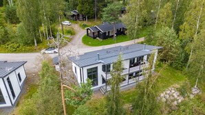 A modern two-story house with a large balcony, surrounded by dense forest.
