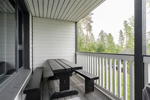 Un espacio al aire libre techado con una mesa de picnic de madera y bancos, barandillas blancas y vistas a árboles.