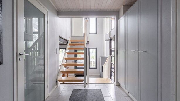 A modern interior with a staircase leading to a balcony, a glass door, and a grey wardrobe.
