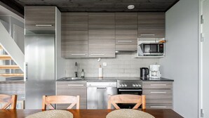 A modern kitchen with grey cabinetry, a stainless steel refrigerator, a microwave, a coffee maker, and a dishwasher. There is a wooden dining table with two woven placemats.