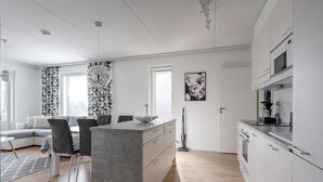 A modern kitchen with white cabinets, a central island, and a dining area with chairs. - Spacious 2BR Apt - Sauna & Lake Views (Jyväskylä)