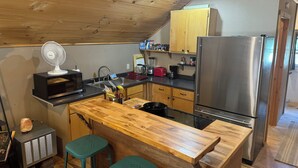 A compact kitchen with wooden cabinets, a stainless steel refrigerator, a microwave, and a wooden island with stools.