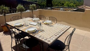 Une table dressée pour quatre personnes sur une terrasse au sol carrelé, entourée de chaises.