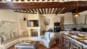 Un salon chaleureux avec une cheminée, un coin repas avec une cuisine en arrière-plan et un mur en pierre.