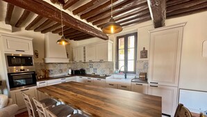 Une cuisine spacieuse avec un grand îlot central en bois, des armoires blanches et un plafond au style rustique.