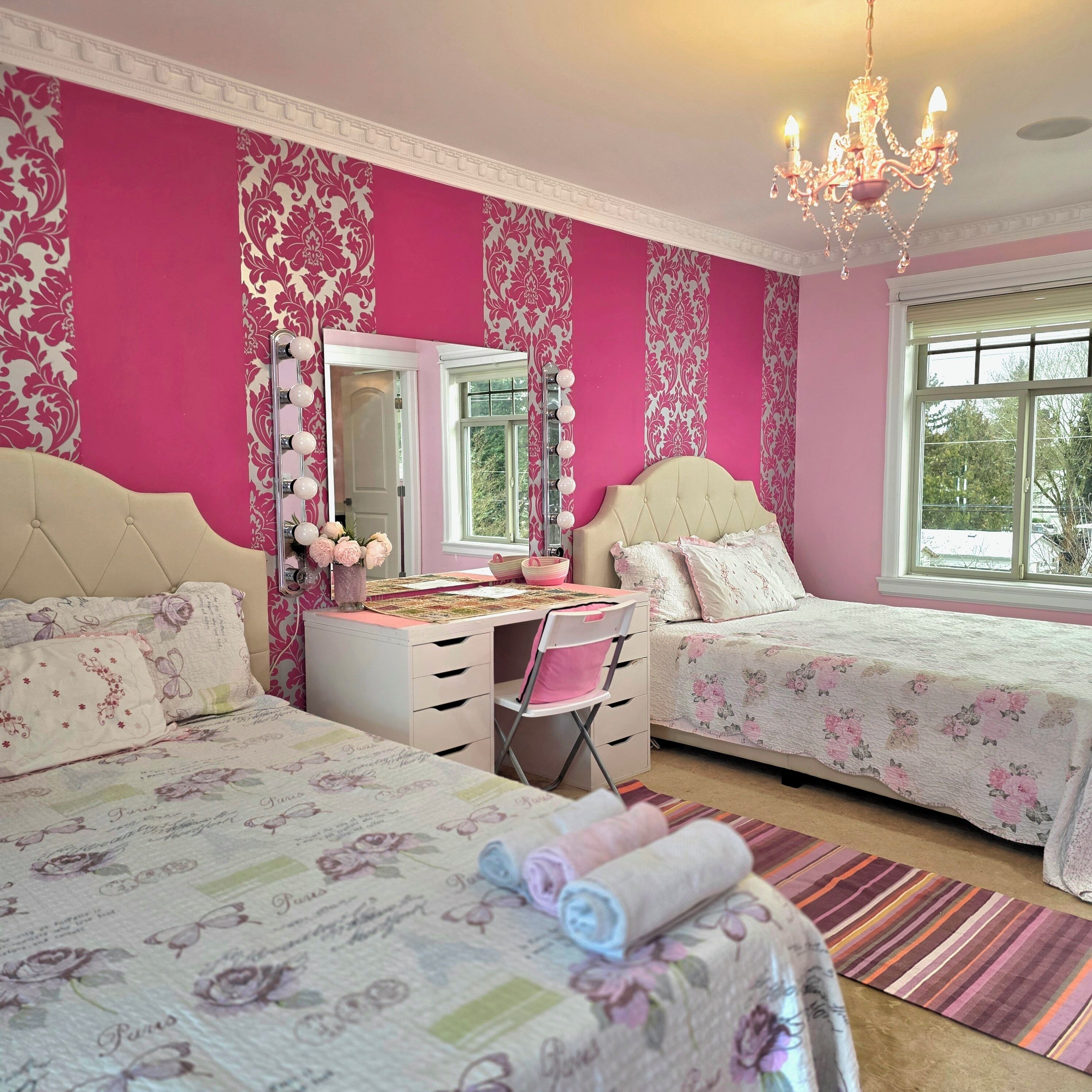A bedroom with two beds, a vanity with a mirror, a chandelier, and a window.