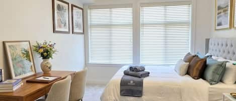 Une chambre à coucher comprenant un lit, une table de chevet, des chaises, un bureau et une fenêtre avec des stores.