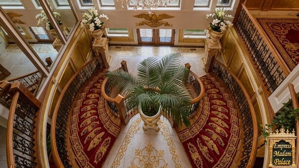 Een statig interieur met een grote kroonluchter, versierde decoraties en een uitzicht op weelderige begroeiing.