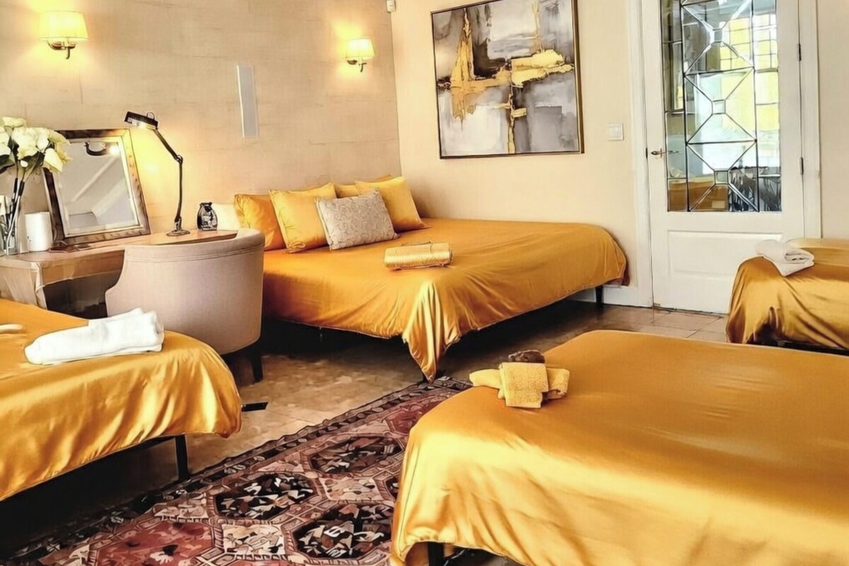A hotel room with two beds, a sitting area, a chandelier, a painting, and a door with a geometric glass design.