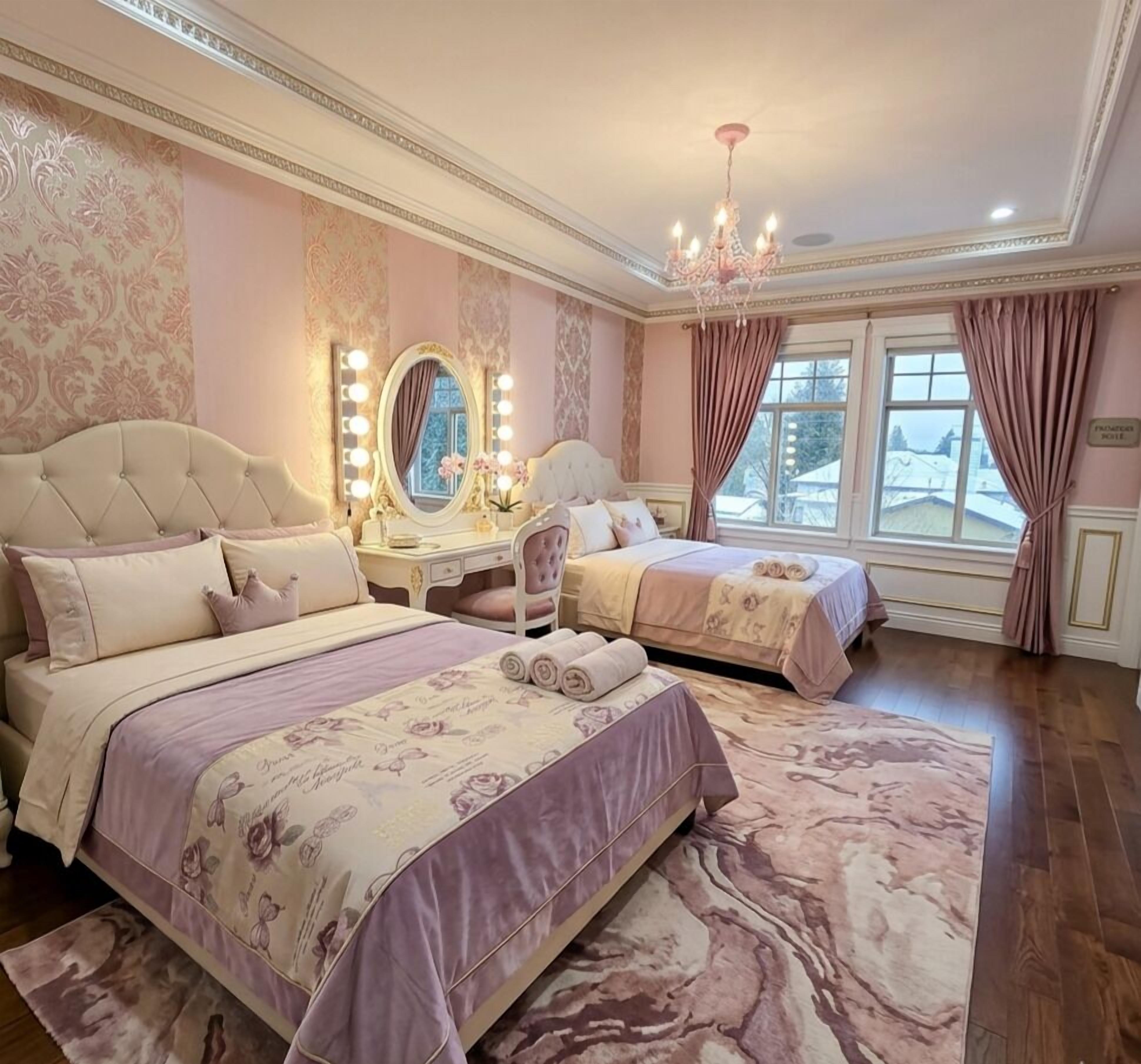 A bedroom with two beds, a vanity with lights, a chandelier, and a view of the outside.
