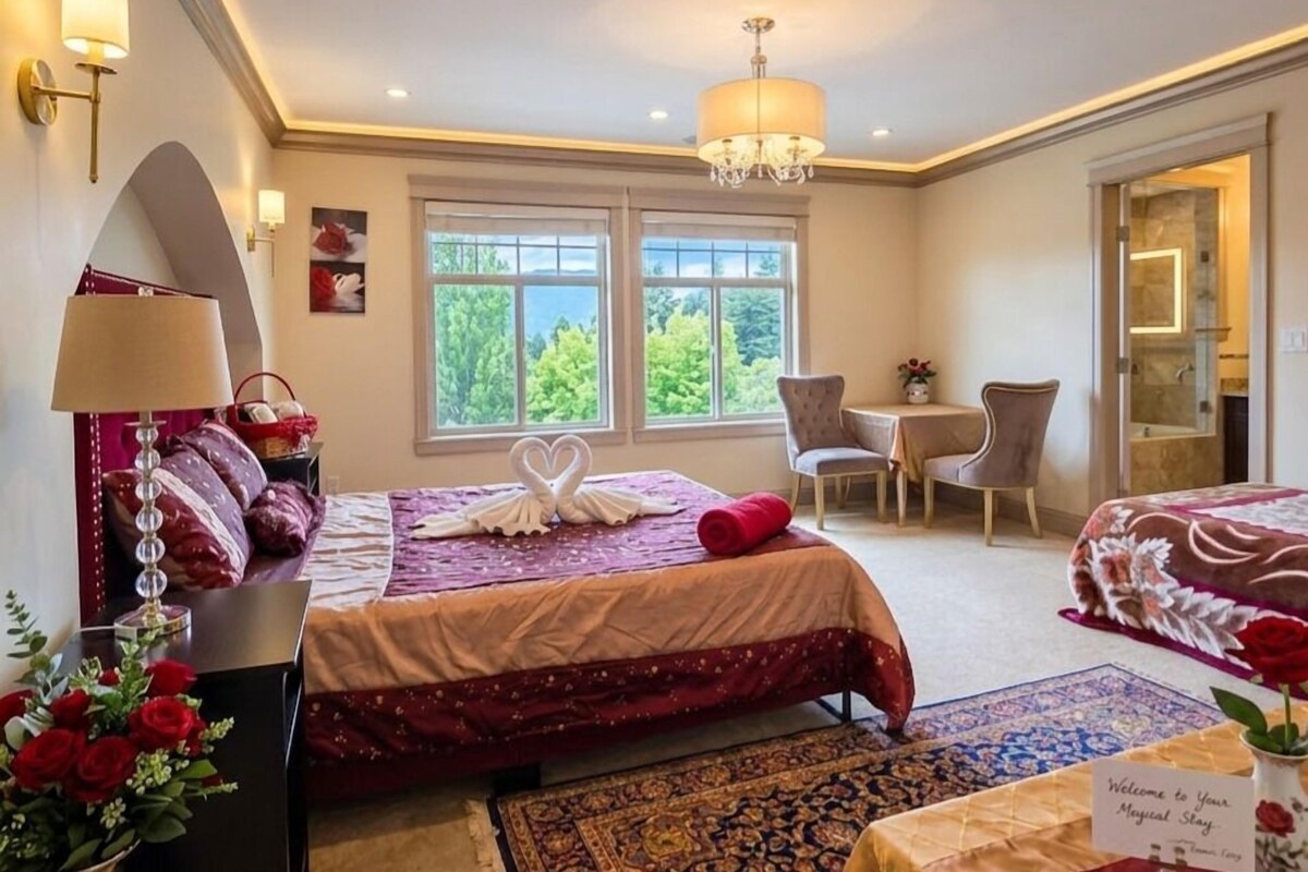 Une chambre d’hôtel avec un lit, un bureau, une chaise, un lustre et une vue sur les arbres par les fenêtres.