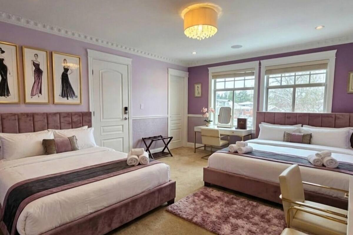 Een slaapkamer met twee bedden, een bureau en een stoel. Er hangen afbeeldingen in lijsten aan de muur, er is een kroonluchter en een raam.