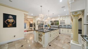 Een luxe keuken met witte kasten, een groot eiland en een kroonluchter.