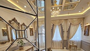 Een luxueuze kamer met een geometrisch glazen scheidingswand, marmeren vloer, weelderige kroonluchters en klassiek interieur.