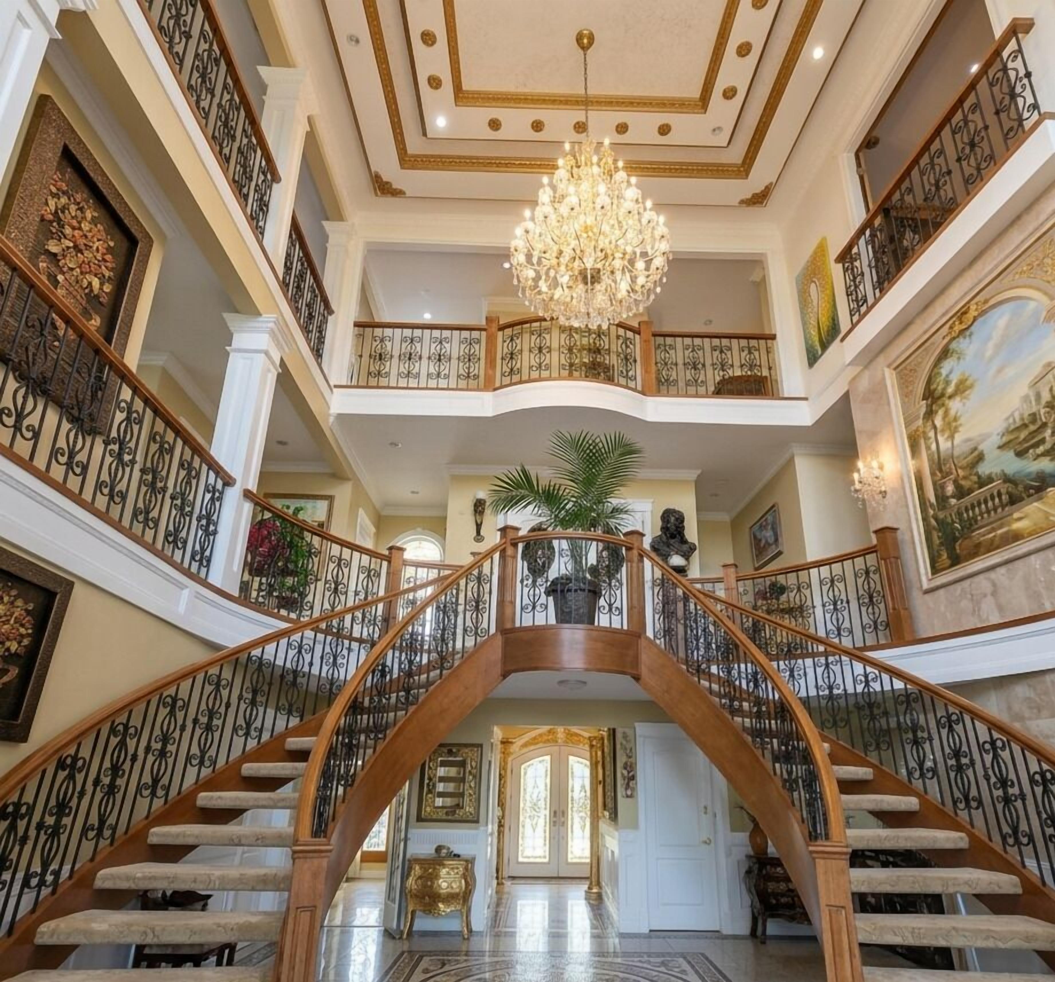 A grand staircase with ornate railings and a chandelier, leading to a second-floor balcony with a view.